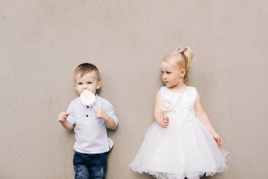 Gri bir arka planda ellerinde şekerlemelerle şık küçük bir çocuk ve kız.