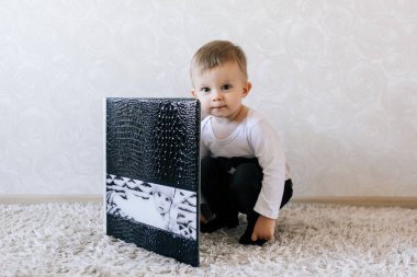 Şirin bebek, büyük şık fotoğraf albümünün yanında oturuyor.