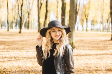 Güzel, mutlu, uzun sarı saçlı, kırmızı dudaklı, şık şapkalı, ceketli, güz sokağında poz veren bir kız. Açık hava portresi, gün ışığı. Kadın sonbahar moda konsepti. 