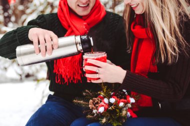 Karlı bir ormanda kış fotoğrafı çekimi aşk hikayesi. Bir erkek ve bir kız termostan sıcak çay dolduruyorlar.