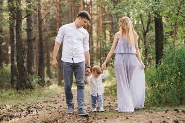 Mutlu genç aile doğada birlikte zaman geçirir. Ebeveynler gider ve çocuğun elini tutar.