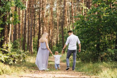 Mutlu genç aile doğada birlikte zaman geçirir. Ebeveynler gider ve çocuğun elini tutar.