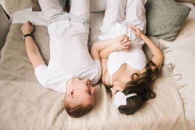 Beyaz elbiseli, sevgi dolu bir çift hafif bir yatakta el ele tutuşuyorlar.