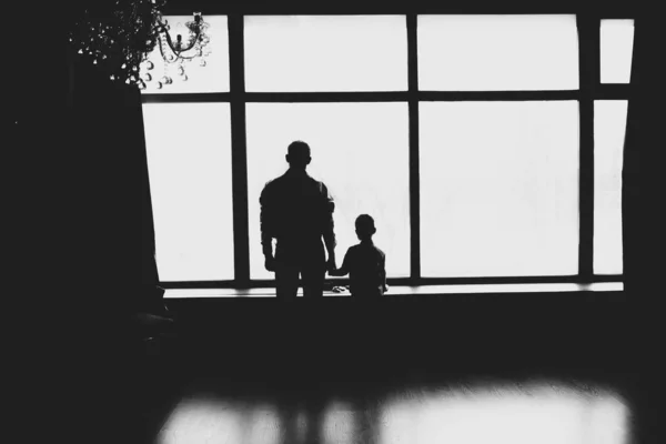 Silhouettes apák és fiúk állnak az ablak mellett. Fekete és mi? — Stock Fotó