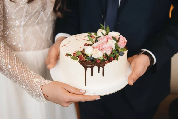 A noiva eo noivo estão segurando um pequeno bolo de casamento decorado w — Fotografia de Stock