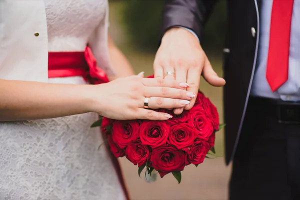 Svatební kytice z rudých růží a ruce novomanželů s — Stock fotografie