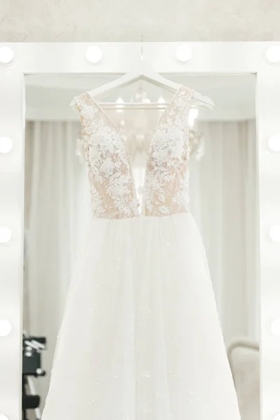 Свадебное платье висит на зеркале, утро невесты — стоковое фото