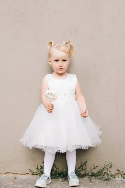 Felice bambina in un vestito bianco con una caramella tra le mani su un — Foto Stock