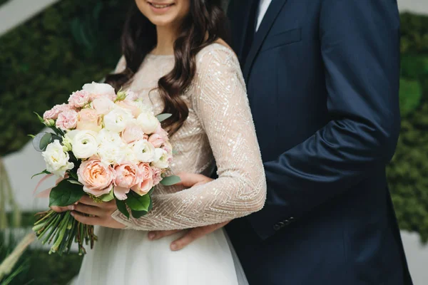 Bruid houdt een bruiloft boeket in handen, de bruidegom hugs haar uit — Stockfoto