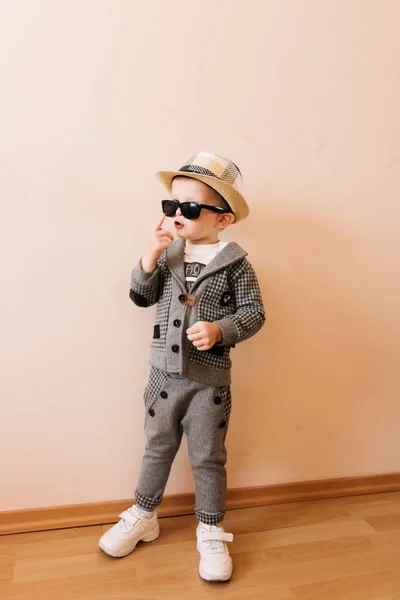 Bébé garçon heureux en costume gris, chapeau et lunettes sur fond clair — Photo