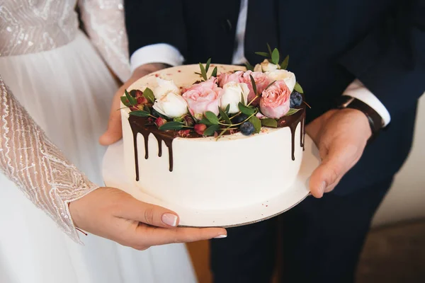 A noiva eo noivo estão segurando um pequeno bolo de casamento decorado w — Fotografia de Stock
