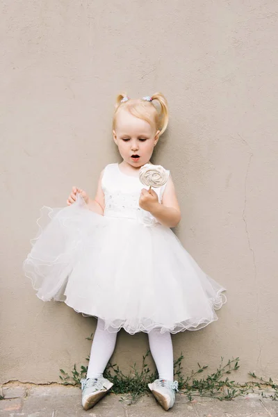 Felice bambina in un vestito bianco con una caramella tra le mani su un — Foto Stock