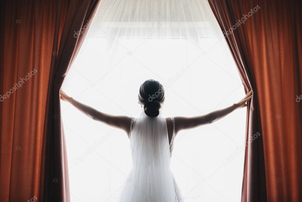 Bride and groom are standing against the window looking outside