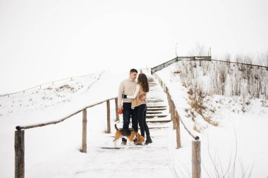 Buzlu kış aşkı hikayesi. Karlı arka planda köpekli şık bir adam ve kız yürüyor