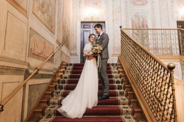 Güzel, zarif, yeni evli çift merdivenlerde lüks bir iç mekanda birbirine aşık.