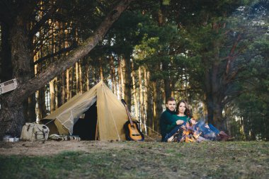 Genç aşıklar kamp yapıyor, kamp ateşinin yanında ormanın içinde çadırın karşısında oturuyorlar. 