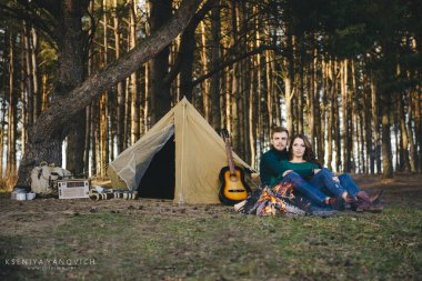 Genç aşıklar kamp yapıyor, kamp ateşinin yanında ormanın içinde çadırın karşısında oturuyorlar. 