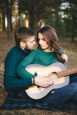 Aşık genç bir çift kamp ateşi başında çadır kurmuş gitar çalıyor.