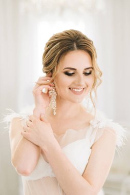 Parlak bir odada romantik bir ortamda genç ve güzel bir gelinin portresi. Gecelikli, düğün saçlı ve makyajlı gelin.