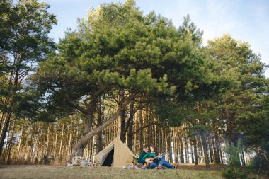 Aşık genç bir çift kamp ateşi başında çadır kurmuş gitar çalıyor.