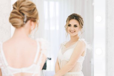 Parlak bir odada romantik bir ortamda genç ve güzel bir gelinin portresi. Gecelikli, düğün saçlı ve makyajlı gelin.