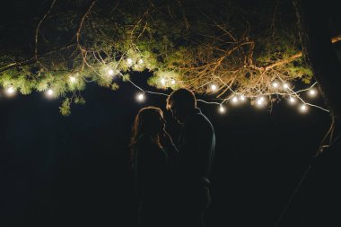 Aşık genç bir çift, ormanda bir çadırın önünde eski bir çelenkle kamp kuruyor. Çok gürültülü bir fotoğraf, seçici bir odak noktası var.