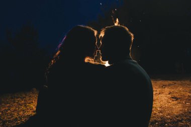 Aşık genç bir çift, ormanda bir çadırın önünde eski bir çelenkle kamp kuruyor. Çok gürültülü bir fotoğraf, seçici bir odak noktası var.