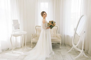 Parlak bir odada romantik bir ortamda genç ve güzel bir gelinin portresi. Bir buket çiçekli gelin.