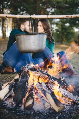 Genç aşıklar kamp yapıyor, kamp ateşinin yanında ormanın içinde çadırın karşısında oturuyorlar. 
