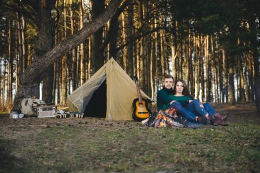Genç aşıklar kamp yapıyor, kamp ateşinin yanında ormanın içinde çadırın karşısında oturuyorlar. 