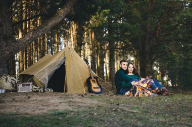 Genç aşıklar kamp yapıyor, kamp ateşinin yanında ormanın içinde çadırın karşısında oturuyorlar. 