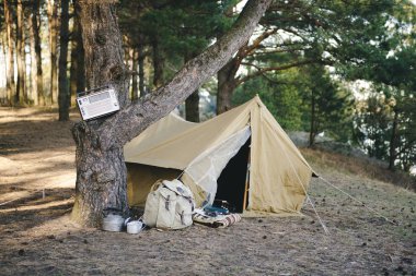 Retro çadır, sırt çantası, gitar, nehir kenarındaki ormanda yangın.