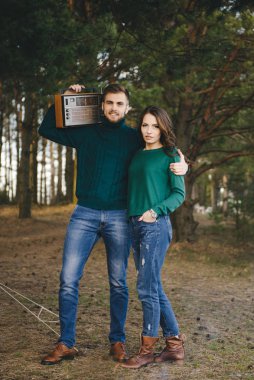 Aşık genç bir çift, kamp yapan turistleri ormandaki bir çadırın önünde oturup retro radyo dinliyorlar.