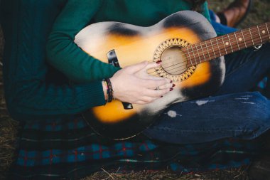 Aşık genç bir çift kamp ateşi başında çadır kurmuş gitar çalıyor.