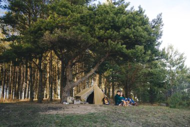 Genç aşıklar kamp yapıyor, kamp ateşinin yanında ormanın içinde çadırın karşısında oturuyorlar. 