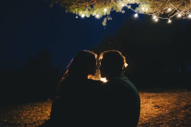 Aşık genç bir çift, ormanda bir çadırın önünde eski bir çelenkle kamp kuruyor. Çok gürültülü bir fotoğraf, seçici bir odak noktası var.