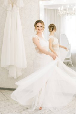 Parlak bir odada romantik bir ortamda genç ve güzel bir gelinin portresi. Gecelikli, düğün saçlı ve makyajlı gelin.