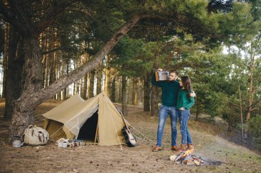 Aşık genç bir çift, kamp yapan turistleri ormandaki bir çadırın önünde oturup retro radyo dinliyorlar.