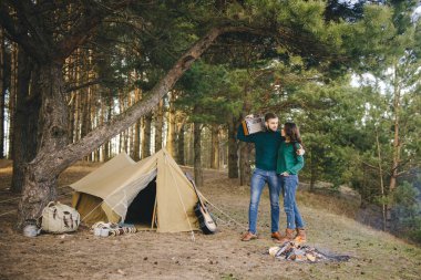 Aşık genç bir çift, kamp yapan turistleri ormandaki bir çadırın önünde oturup retro radyo dinliyorlar.