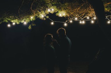 Aşık genç bir çift, ormanda bir çadırın önünde eski bir çelenkle kamp kuruyor. Çok gürültülü bir fotoğraf, seçici bir odak noktası var.