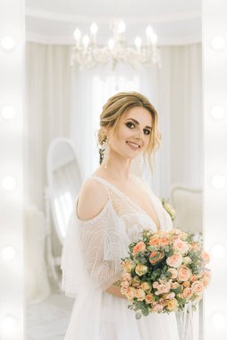 Parlak bir odada romantik bir ortamda genç ve güzel bir gelinin portresi. Bir buket çiçekli gelin.