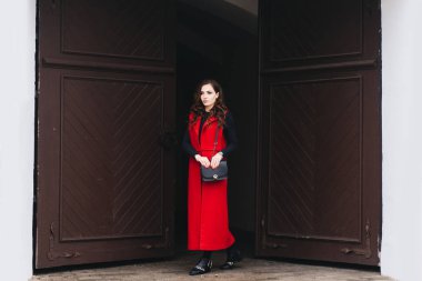 Siyah elbiseli ve uzun kırmızı yelekli eski bir şehrin sokaklarında şık bir genç kızın açık hava portresi. Bir Avrupa şehrinin caddesinde bir model poz veriyor