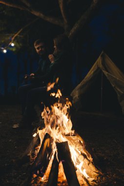 Aşık genç bir çift, ormanda bir çadırın önünde eski bir çelenkle kamp kuruyor. Çok gürültülü bir fotoğraf, seçici bir odak noktası var.