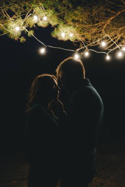 Aşık genç bir çift, ormanda bir çadırın önünde eski bir çelenkle kamp kuruyor. Çok gürültülü bir fotoğraf, seçici bir odak noktası var.