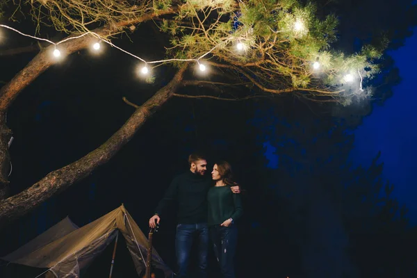 Aşık genç bir çift, ormanda bir çadırın önünde eski bir çelenkle kamp kuruyor. Çok gürültülü bir fotoğraf, seçici bir odak noktası var.