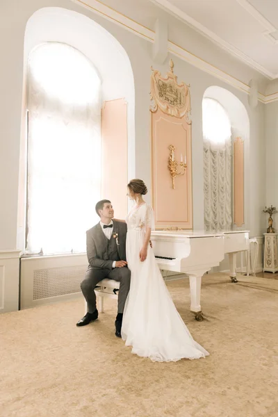 ピアノの近くの豪華なインテリアで恋に新婚夫婦の美しいエレガントな — ストック写真