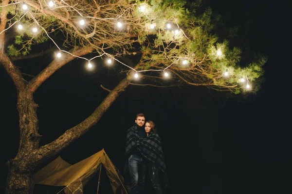 Aşık genç bir çift, ormanda bir çadırın önünde eski bir çelenkle kamp kuruyor. Çok gürültülü bir fotoğraf, seçici bir odak noktası var.