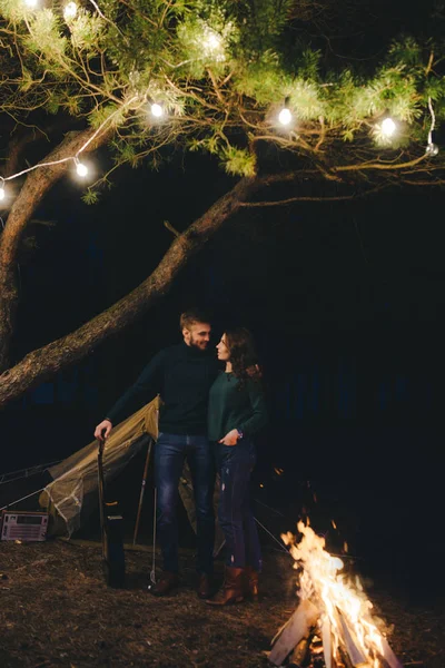 Aşık genç bir çift, ormanda bir çadırın önünde eski bir çelenkle kamp kuruyor. Çok gürültülü bir fotoğraf, seçici bir odak noktası var.