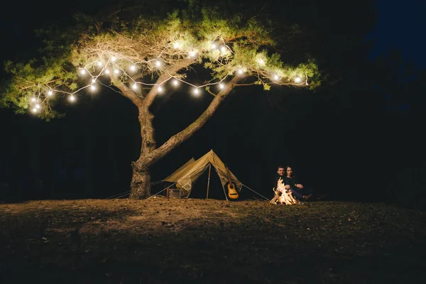 Aşık genç bir çift, ormanda bir çadırın önünde eski bir çelenkle kamp kuruyor. Çok gürültülü bir fotoğraf, seçici bir odak noktası var.