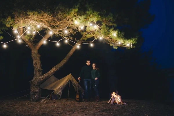 Aşık genç bir çift, ormanda bir çadırın önünde eski bir çelenkle kamp kuruyor. Çok gürültülü bir fotoğraf, seçici bir odak noktası var.